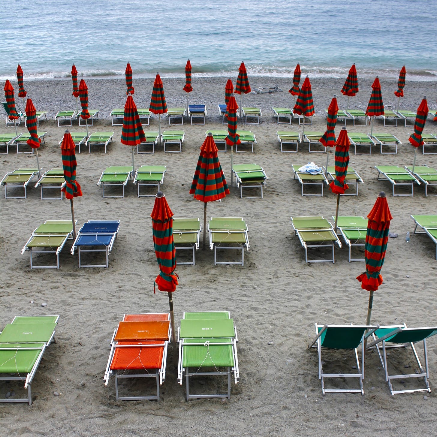 sets of green and orange umbrellas over colorful chairs on a beach.