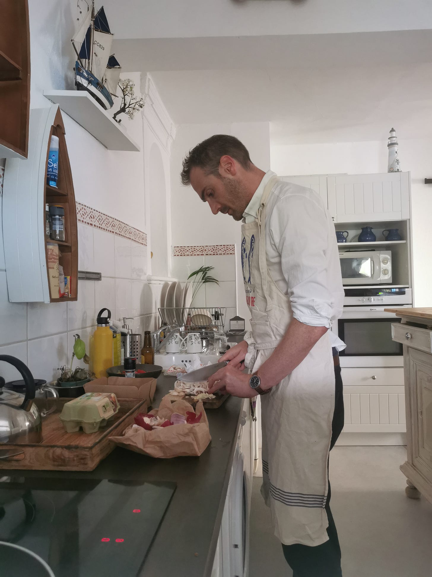 A man in a white shirt and apron chops mushrooms on a kitchen worktop.