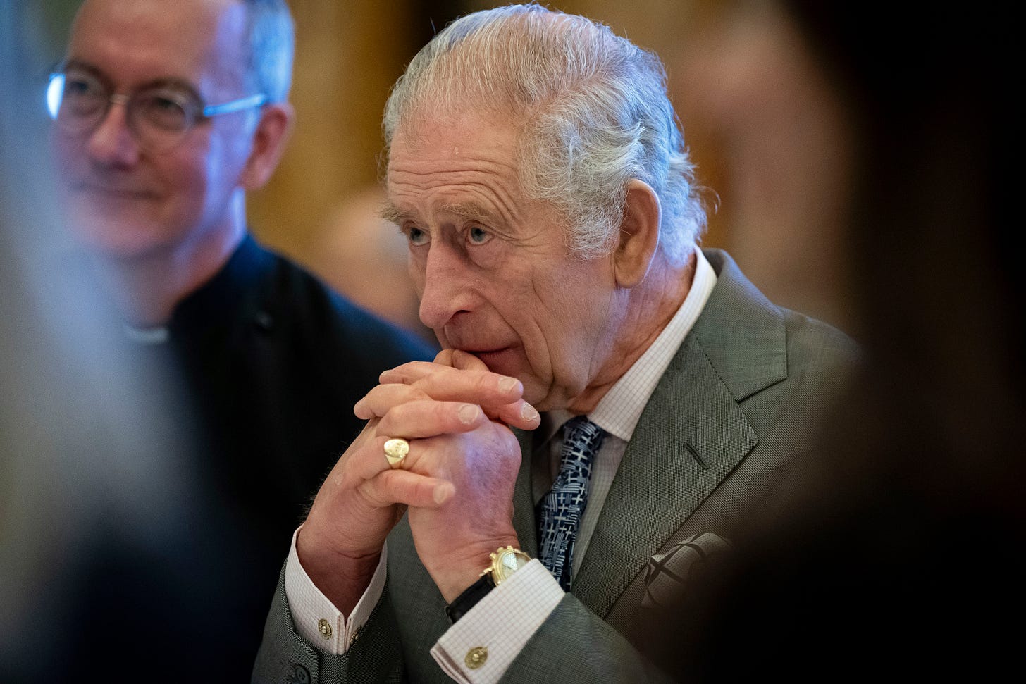 King Charles III sits with his chin resting on his folded hands.