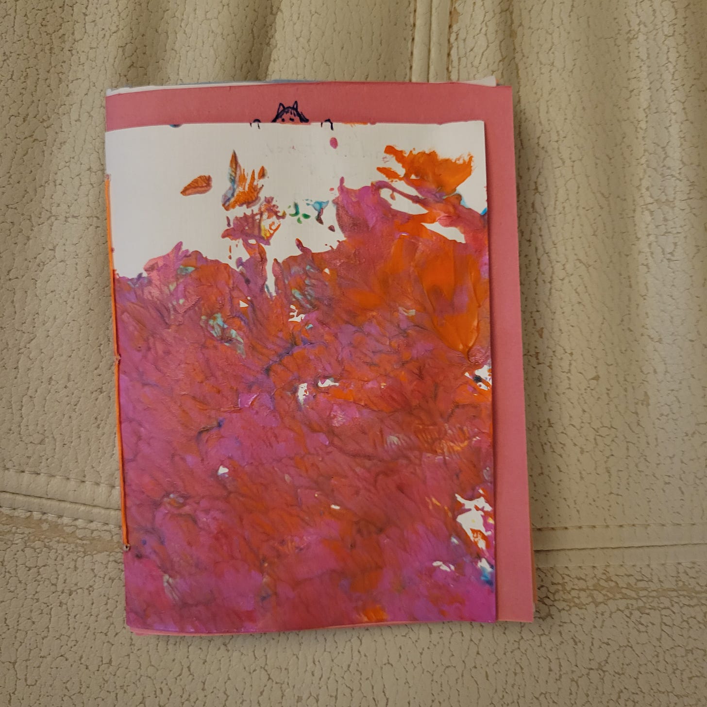closed booklet with orange stitching and a hand painted cover in pink
