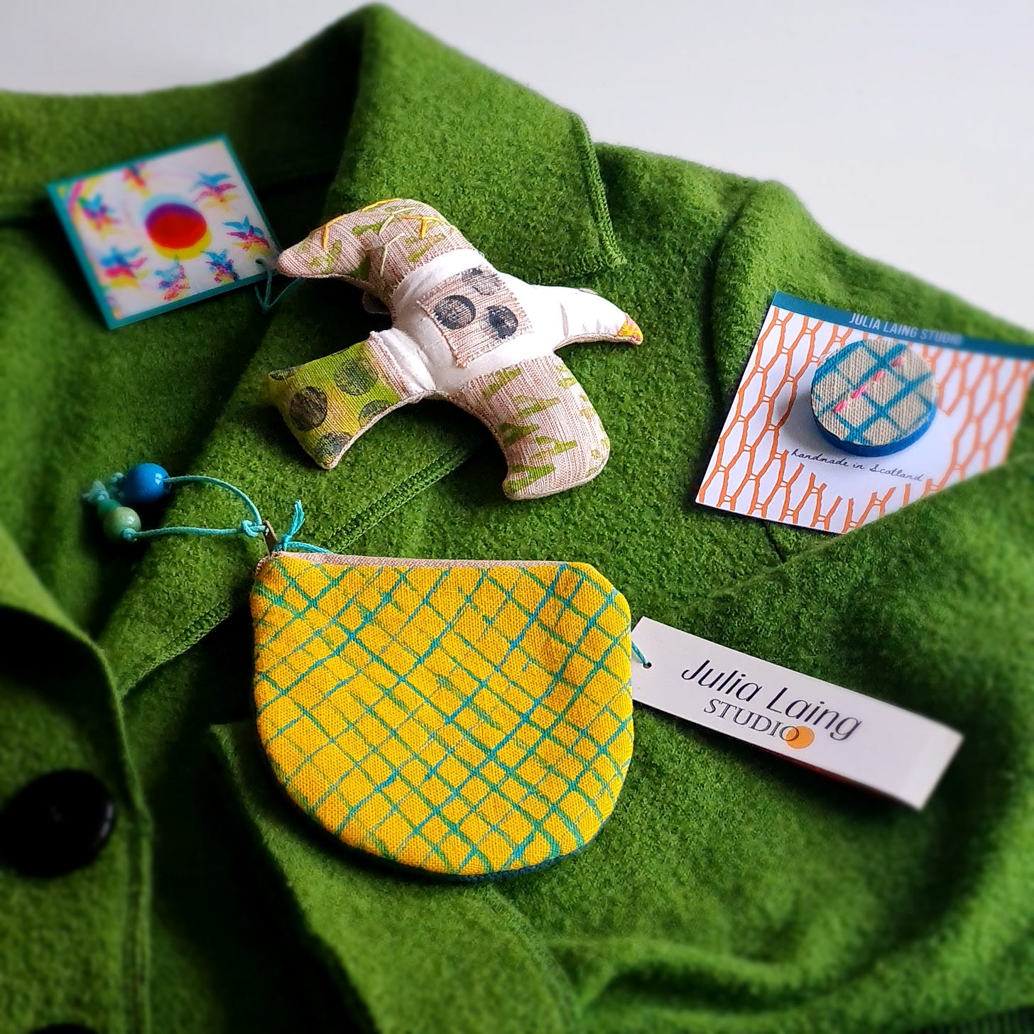 Handmade textles by Julia Laing lying on a bright green wool jacket on a white table.