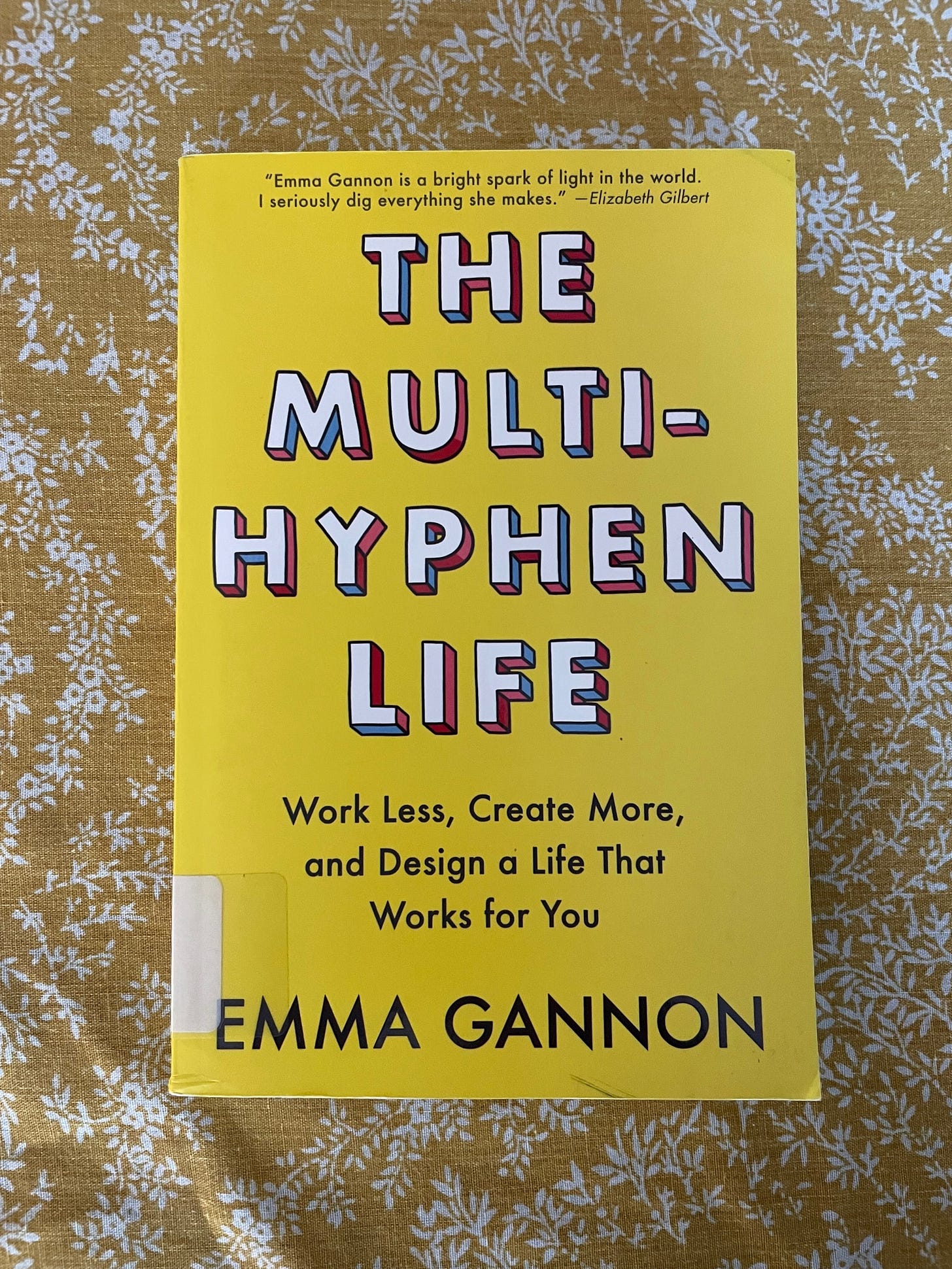 Emman Gannon's book "The Multi-Hyphen Life: Work Less, Create More, and Design a Life That Works for You" is sitting on a yellow floral background