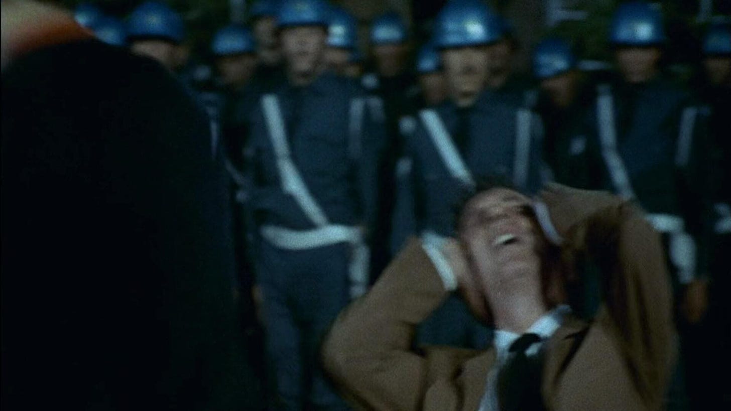 A still from Costa-Gavras's Z featuring a politician holding his head down after having been hit with a club.
