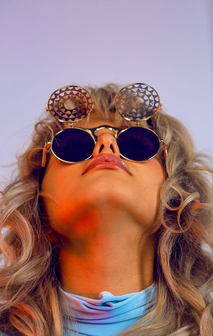 girl with long blonde hair looking up through round sunglasses with flipped up shade covers