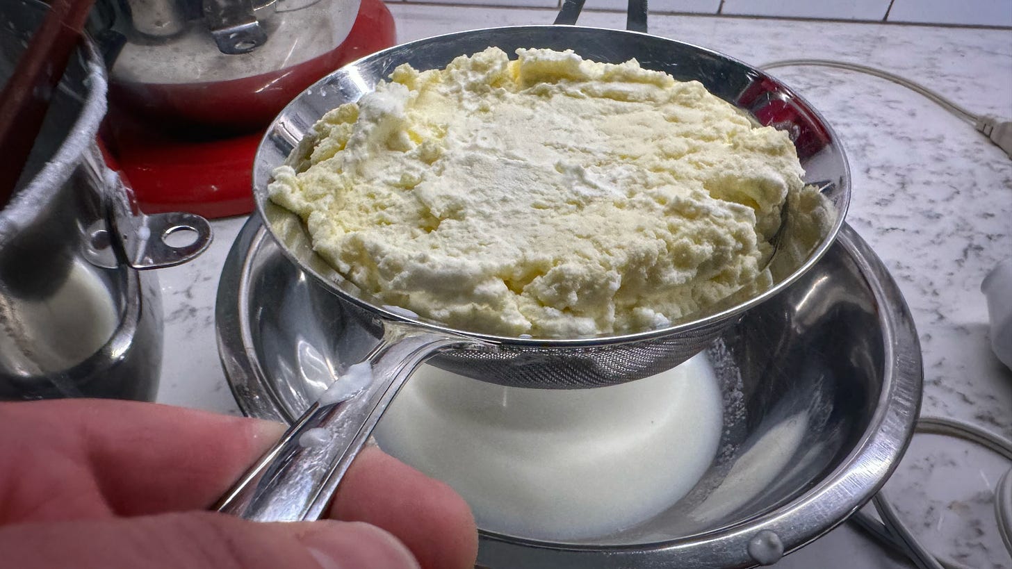 The newly-made butter being drained in a fine-meshed sieve held over a steel mixing bowl. Buttermilk has collected in the bowl.
