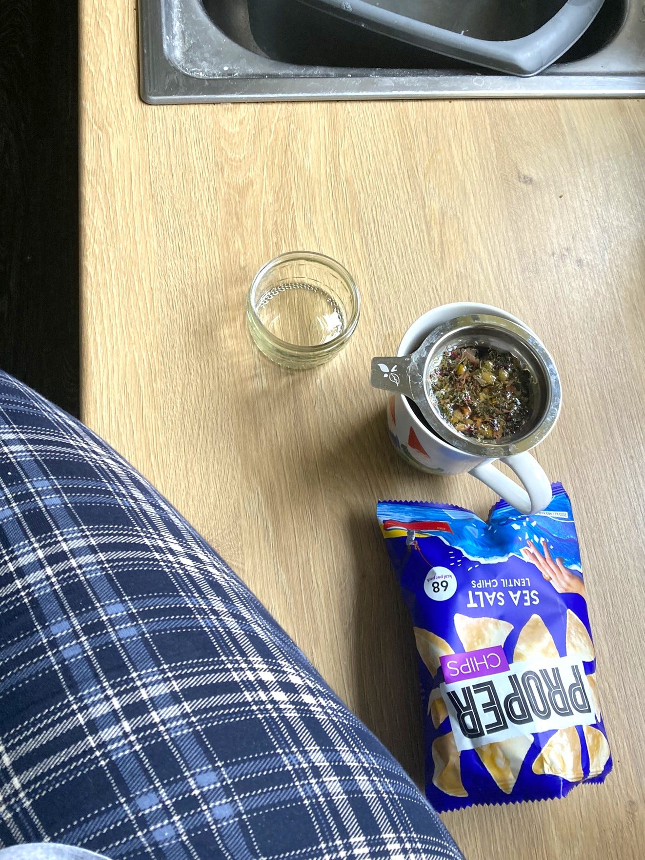 A pyjama-clad leg can be seen in the bottom left corner. She's sat on the kitchen counter with a packet of lentil crisps and a mug of loose leaf tea brewing.