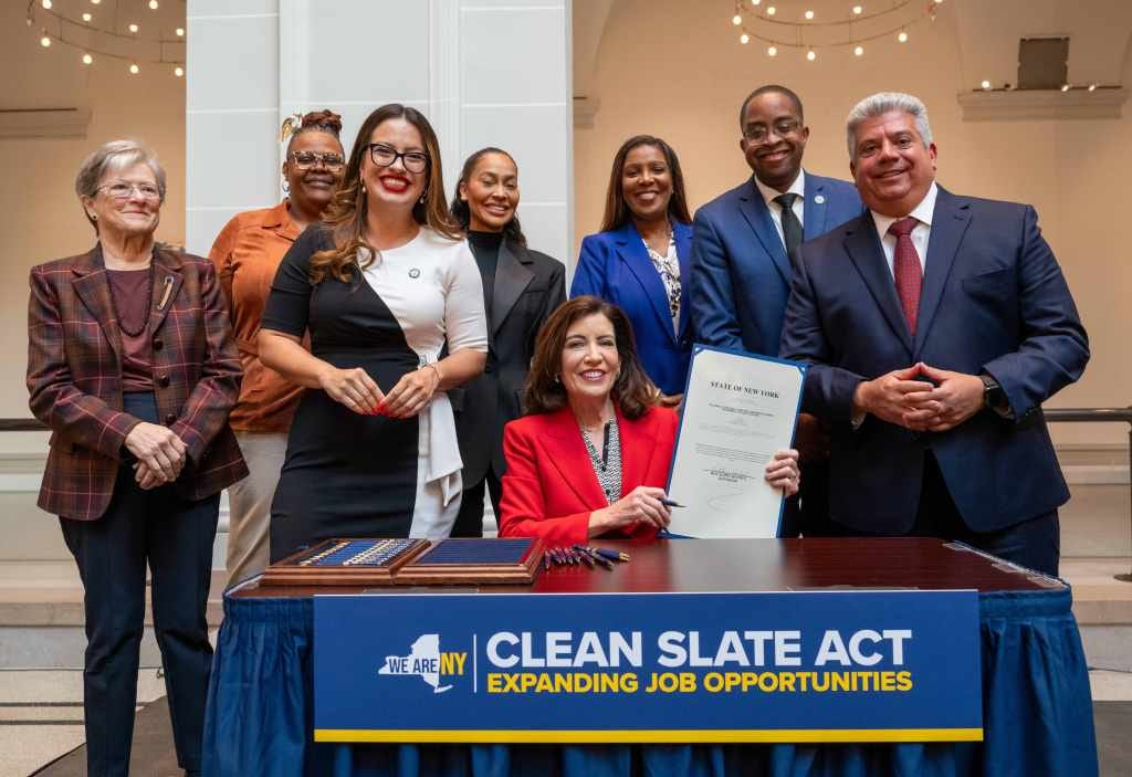 Gov. Kathy Hochul holds the signed "Clean Slate Act" surrounded by lawmakers, the attorney general and community advocates.