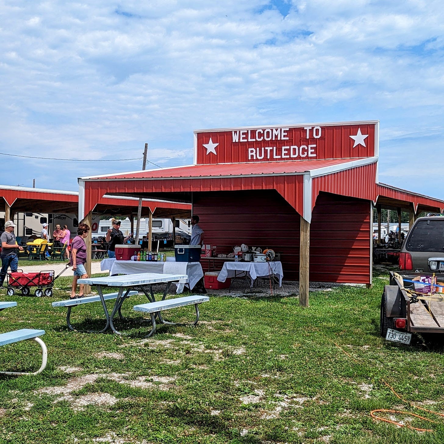 A red shed with a 'Welcome to Rutledge' sign, and a few food items for sale next to some picnic tables