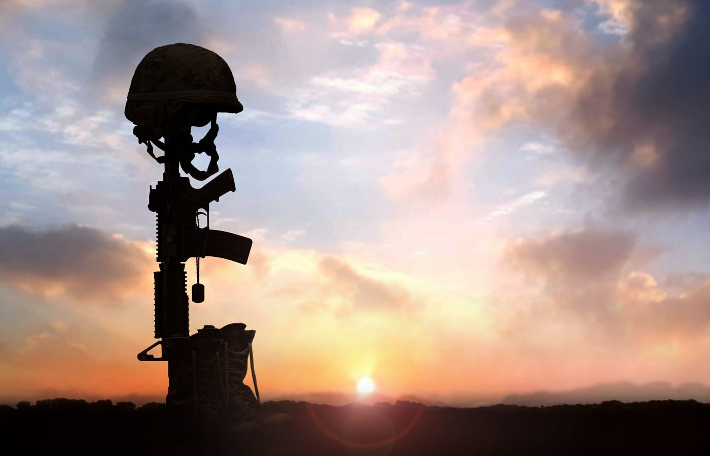 A dead soldier’s boots, rifle, dog tags, and helmet arranged as a standing memorial and silhouetted by the setting sun