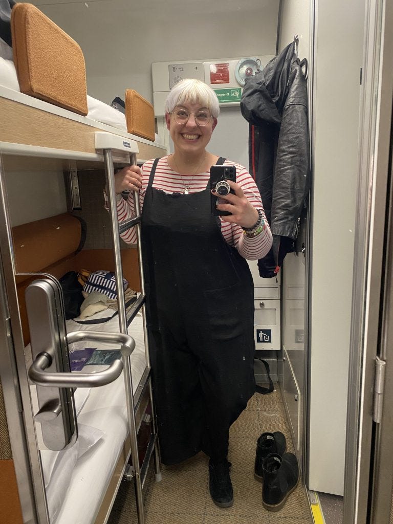 A woman grins while taking a photo of herself in the mirror in the door of a train sleeper cabin