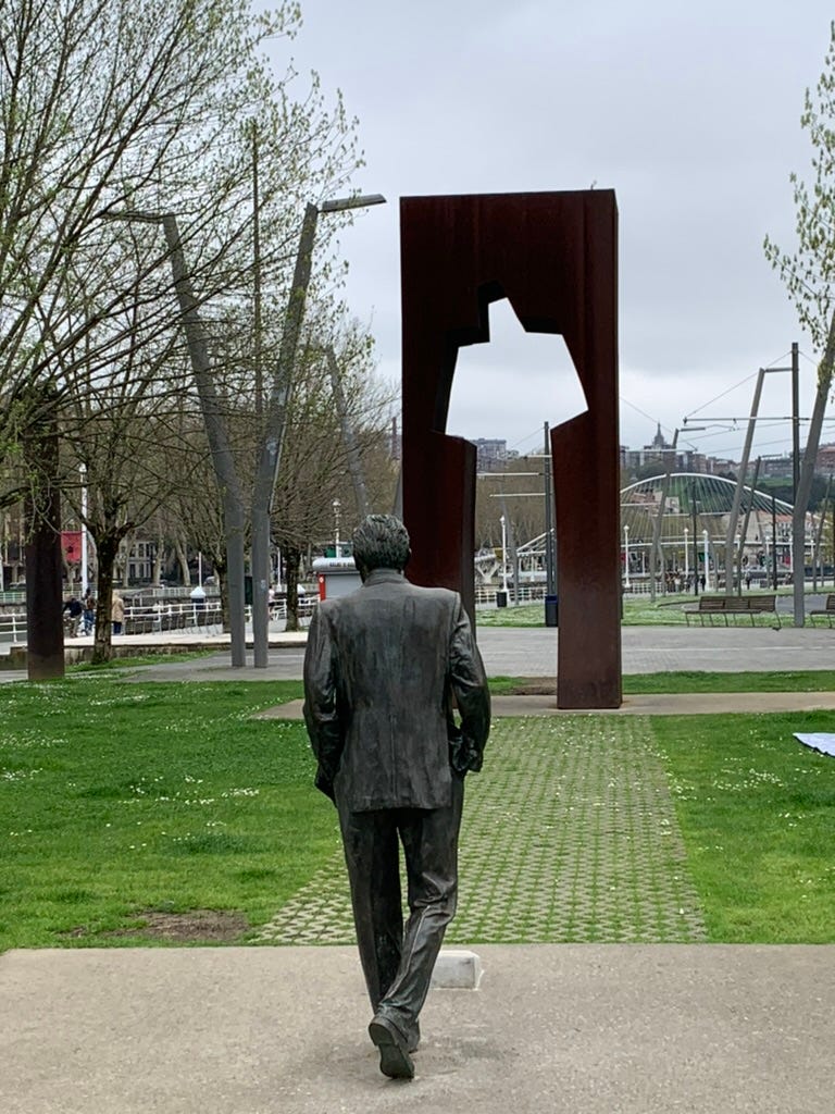 A sculpture of a man walking towards a cutout of a blocky man-shaped hole in a giant slab of metal.