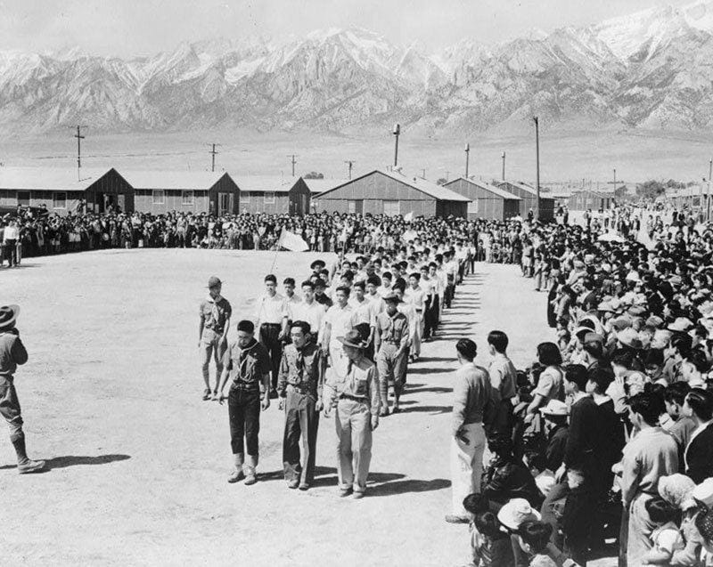 Columns of Japanese-American citizens at the Manzanar concentration camp stand in lines before a soldier shouting at them.