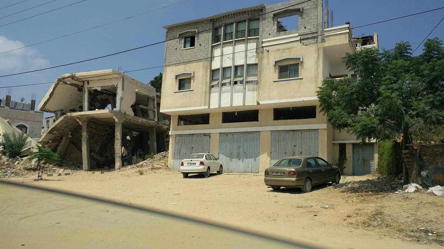 A half-collapsed, gutted building stands next to another with cars in front of it