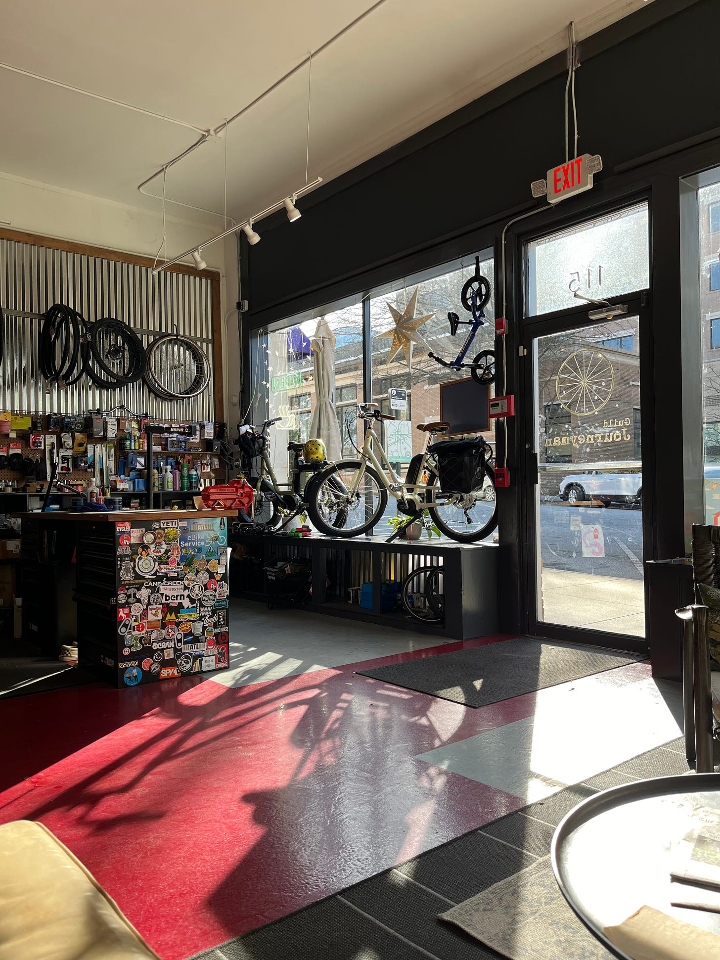 Image from inside Guild + Journeyman, showing bikes hanging on the wall and bumper stickers all over the furniture and sunlight streaming through the front windows.