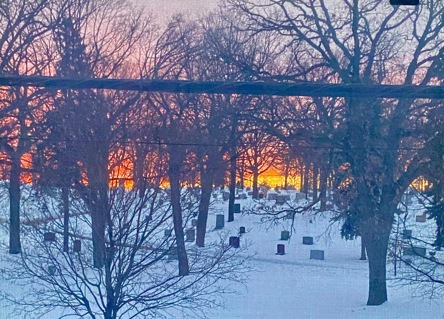 Sunset, through a window, over a snowy cemetery