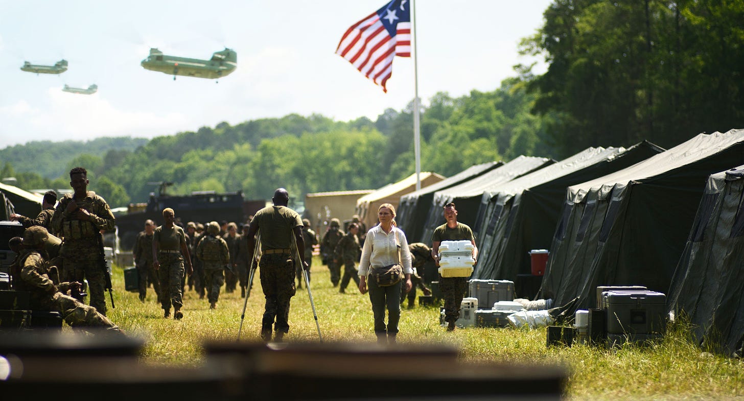 Kirsten Dunst walking through an open field with soldiers tents a military planes flying overhead