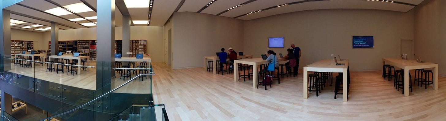 A panorama of the upper level of San Francisco's Apple Store. The former Theater space contains tables, black stools, and small monitors on the wall. The walls have been painted white. 