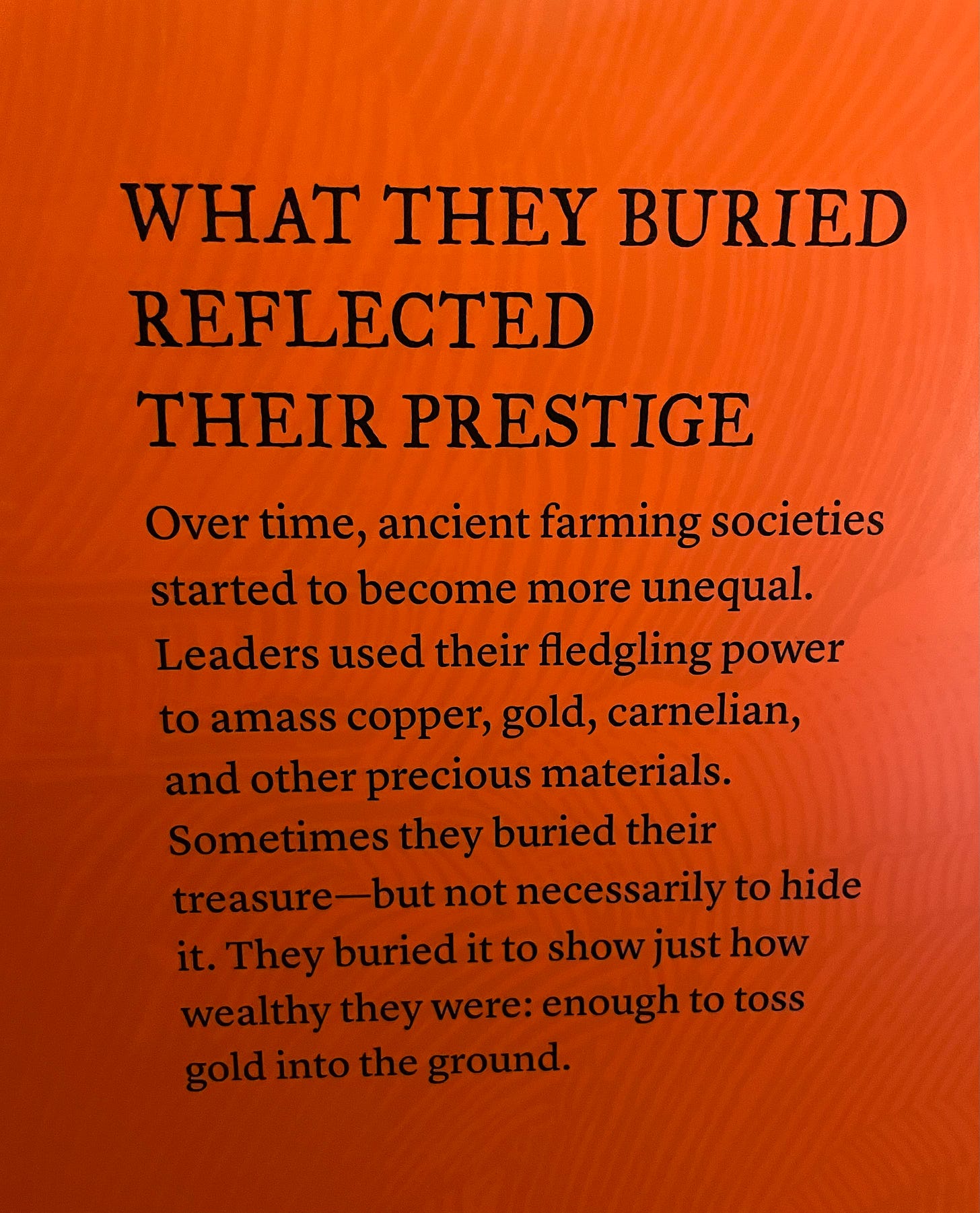 museum plaque reading 'what they buried reflected their prestige. Over time, ancient farming societies started to become more unequal. Leaders used their fledgling power to amass copper, gold, carnelian, and other precious materials. Sometimes they buried their treasure—but not necessarily to hide it. They buried it to show just how wealthy they were: enough to toss gold into the ground'