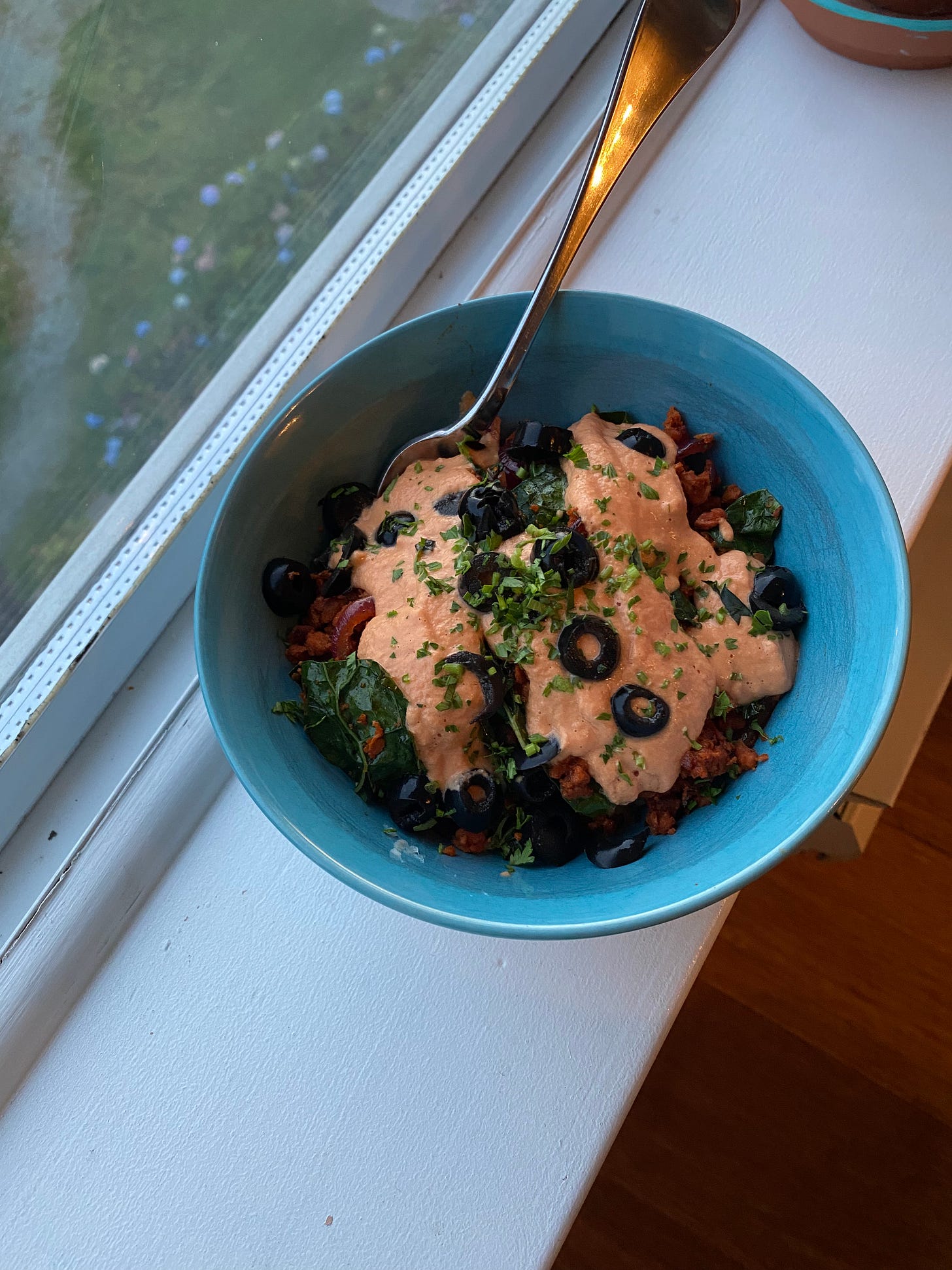 On the windowsill, a blue bowl of the rice, sausage mix, olives, and sauce described above.