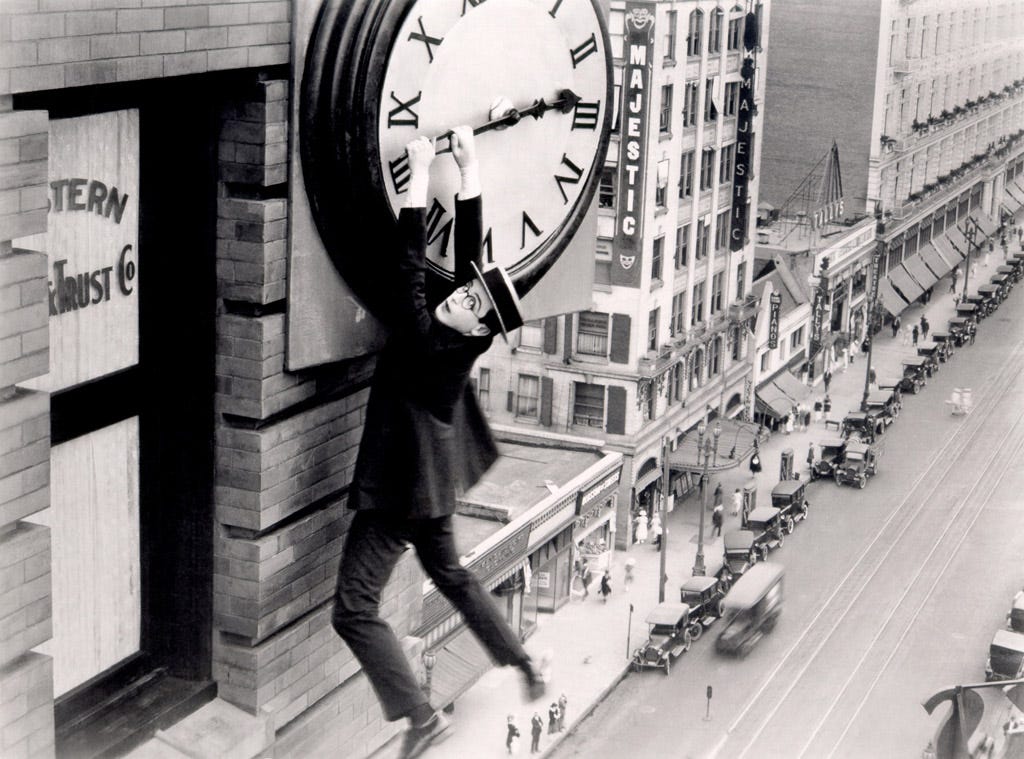 Black and white photo of a man hanging from a clock hand atop a building