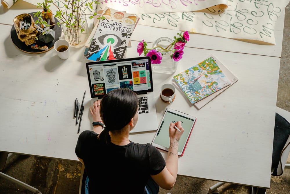 Woman sitting at computer and iPad drawing and and looking at multiple things