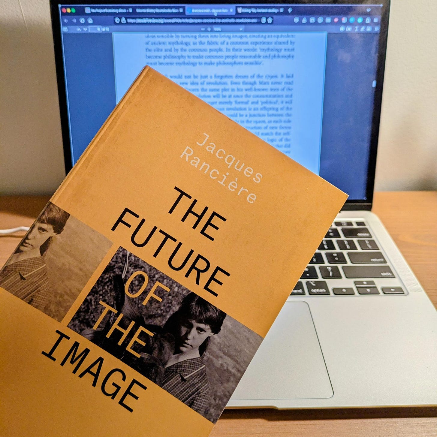 Photo of a laptop computer out of focus with a text on the screen, in front of which is the book "The Future of the Image" with a bright yellow cover.