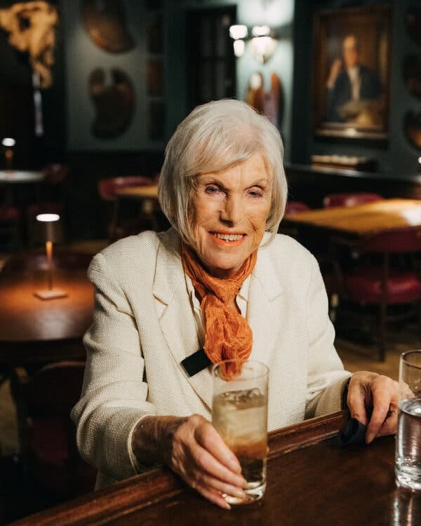 An older woman sits at a bar holding a drink.