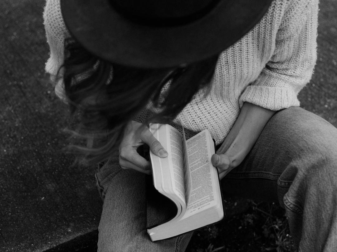 woman sitting on ground while opening book