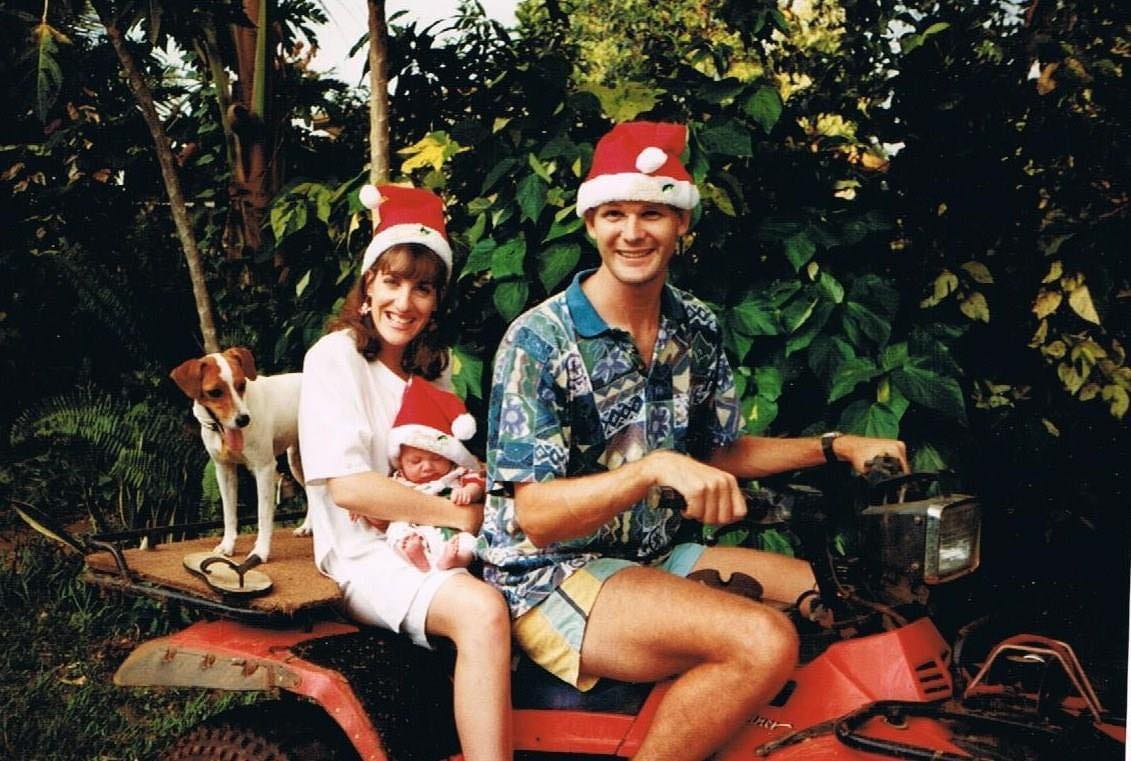 A young mother, father and newborn baby on a red 4 wheel motorbike with their jack russel dog and christmas hats