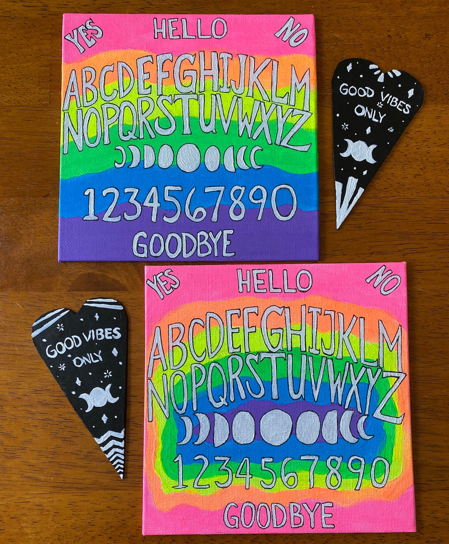Two small neon rainbow Ouija boards with black and white planchettes