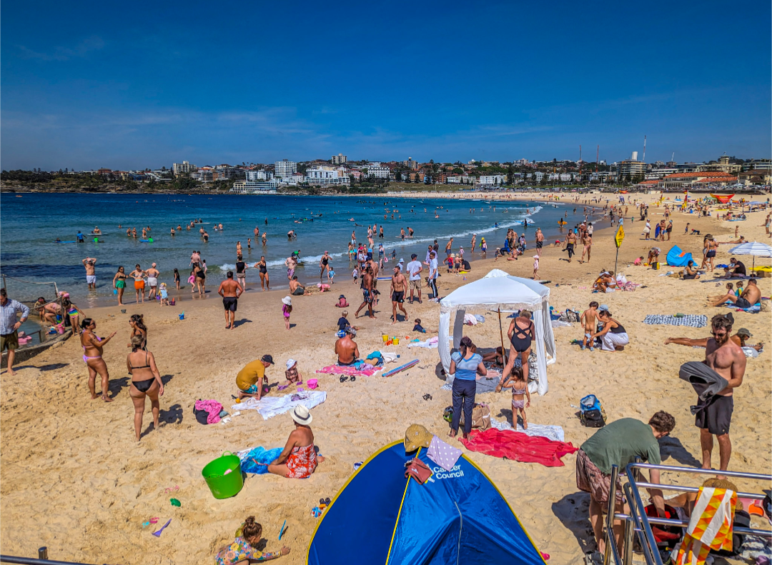 A busy Bondi Beach on a sunny day, the golden sand filled with folks in swimsuits.