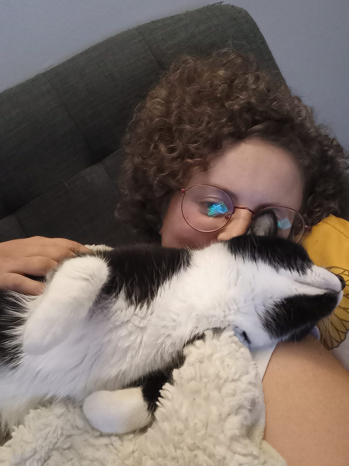 Alyssa curled up on the couch with Dooty, a tuxedo cat with her belly to the air