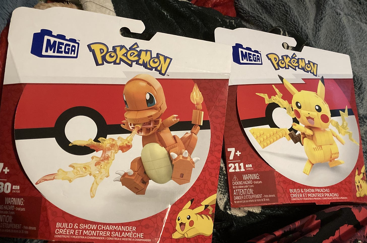 Two boxes containing Pokémon Mega Bloks kits, one is Charmander breathing fire, and the other is Pikachu letting out sparks from his cheek pouches. 