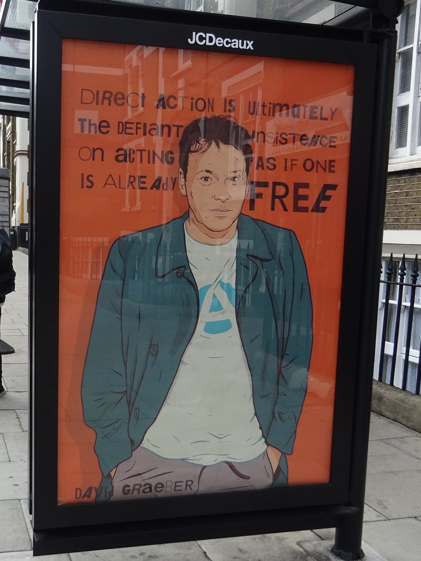 A poster on a bus stop that reads: Direct action is, ultimately, the defiant insistence on acting as if one is already free, a quote by David Graeber