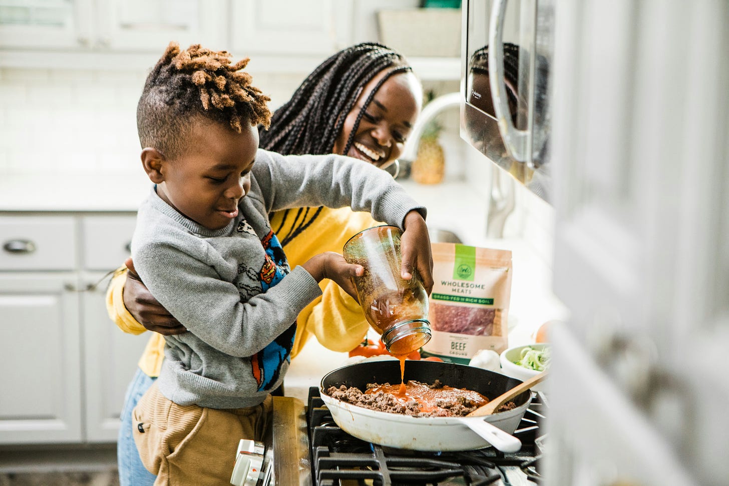 African American boy in gray long sleeve shirt cooking at a stove with his mom