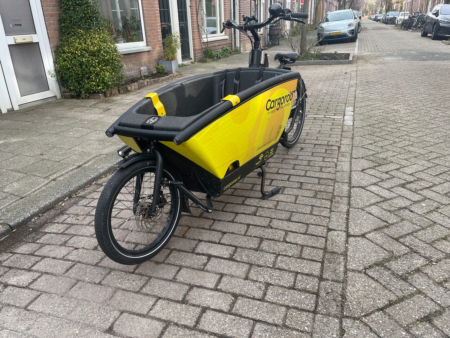 A yellow Cargoroo cargobike is parked in a car parking bay on a residential dutch street