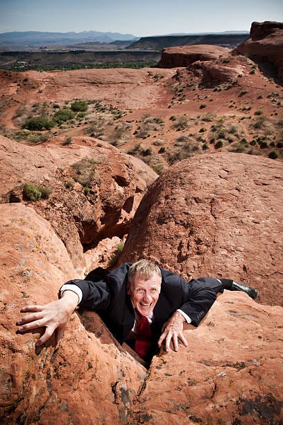 Businessman Climbing Up Rockface Mature man in suit struggling up from red rock crevasse. men struggle rock climbing mountain climbing stock pictures, royalty-free photos & images