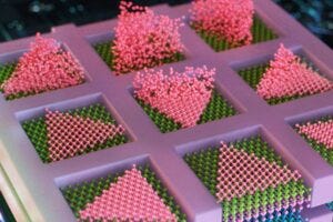 MIT engineers have developed a method to seamlessly stack electronic layers to create faster, denser, more powerful computer chips. The team deposits semiconducting particles (in pink) as triangles within confined squares, to create high-quality electronic elements, directly atop other semiconducting layers (shown in layers of purple, blue, and green). Credits:Credit: Cube 3D Graphic