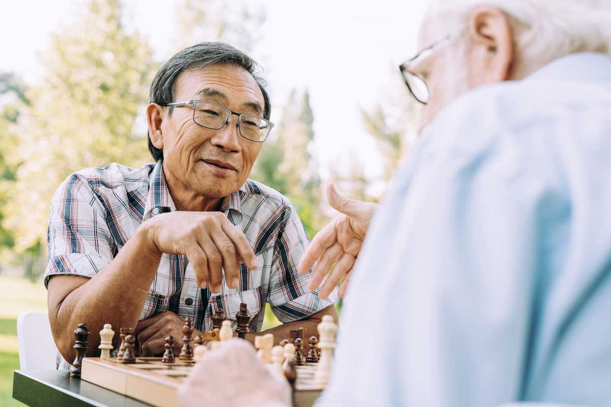 Two elder friends laughing over a game of chess in the park.