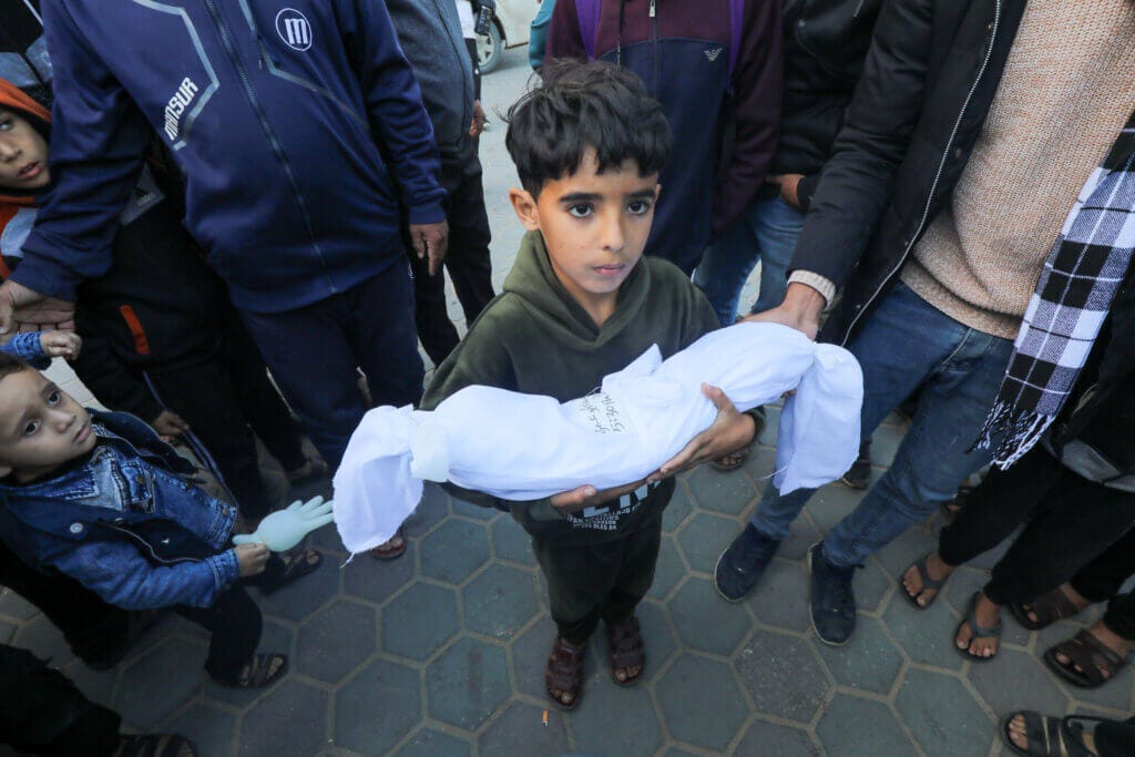 A young Palestinian boy holds the shrouded body of a Palestinian infant who was killed by Israeli airstrikes in Gaza in Deir al-Balah in the central Gaza Strip. (APA Images)