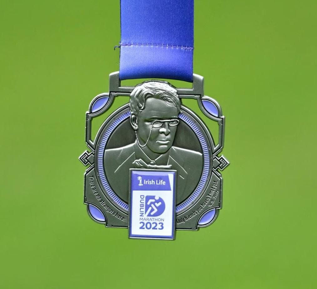 Pewter-coloured square Dublin Marathon medal on a blue ribbon and green background depicting W.B. Yeats