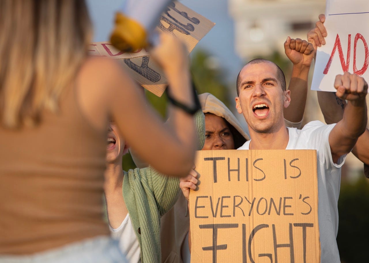Close up angry people at protest. with a man holding a sign saying "this is everyon's fight"