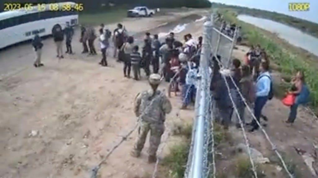 Footage showing migrants who'd just entered through open gate waiting to get onto a white bus.