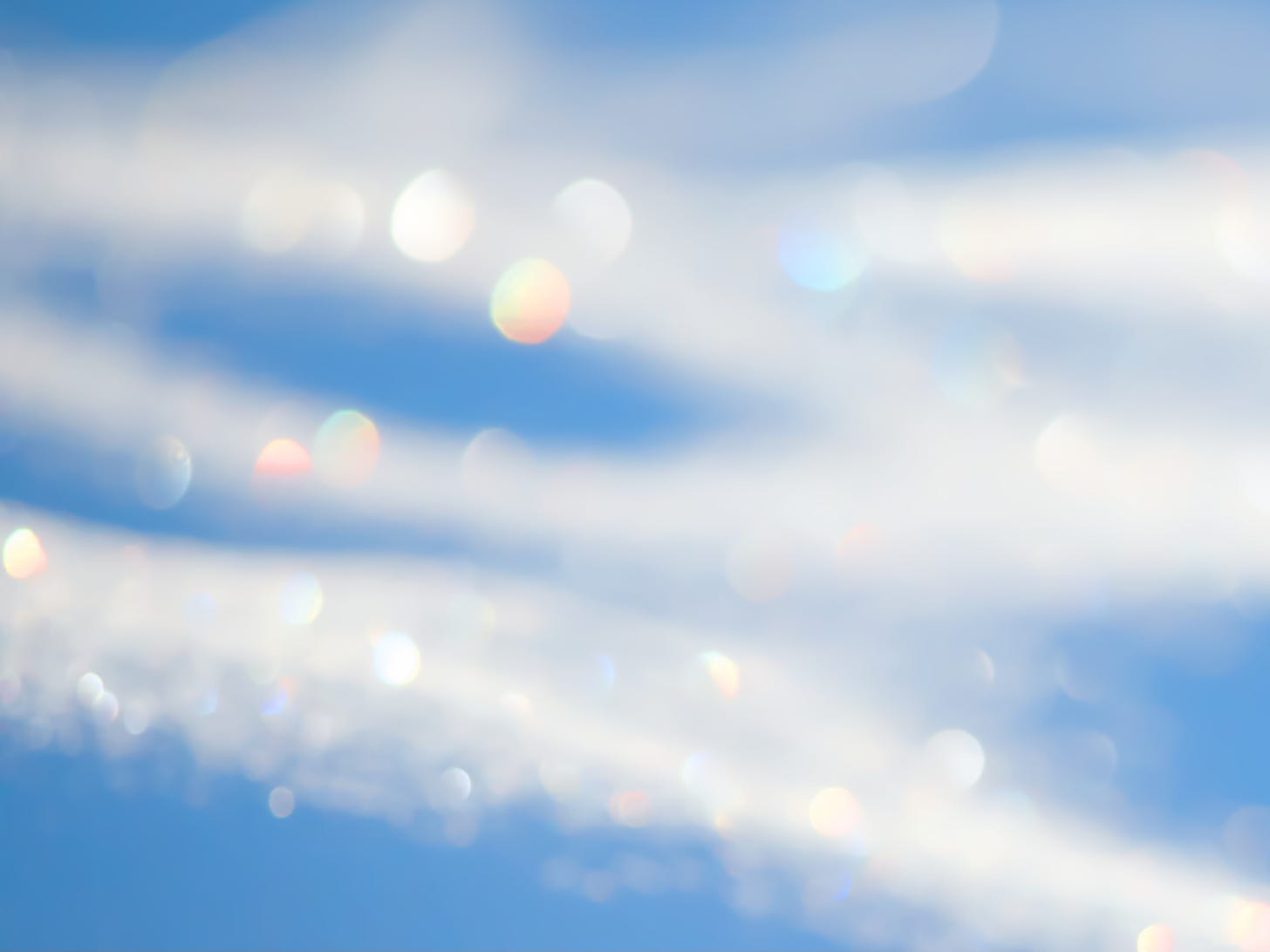 An abstract images uses a soft focus on snow, with blue shadows, white highlights, and rainbow bokeh.