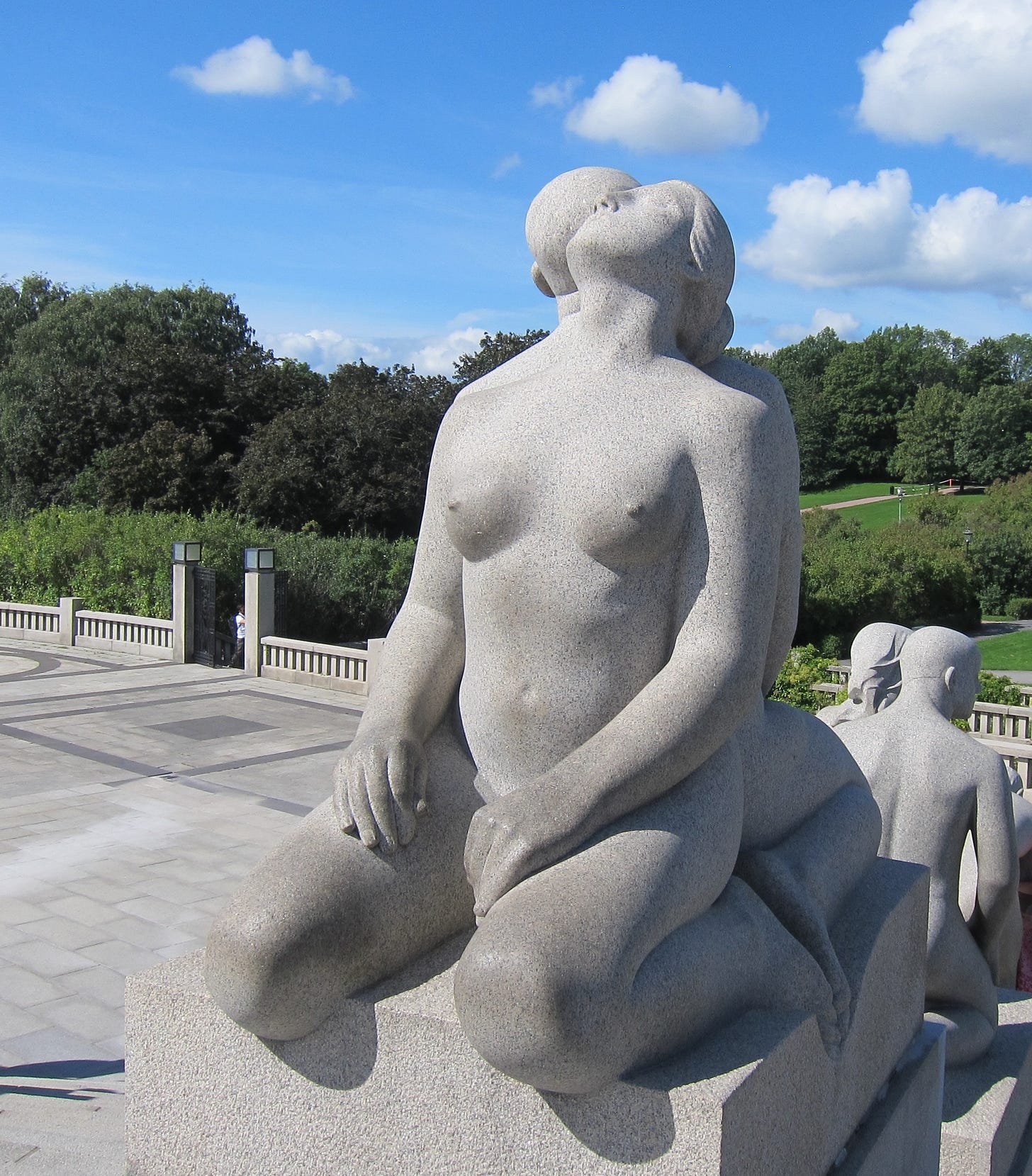 granite statue of two humans back to back leaning their heads against each others shoulder against a blue sky