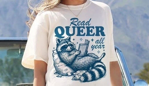 a tee shirt with an illustration of a raccoon reading and the text Read Queer All Year