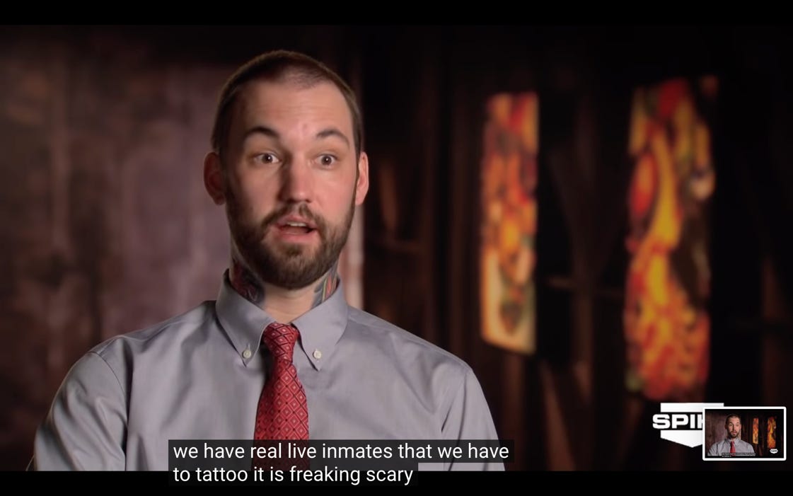 A tattooed man with a beard and a tie, looking shocked, saying "we have real live inmates that we have to tattoo it is freakin scary."
