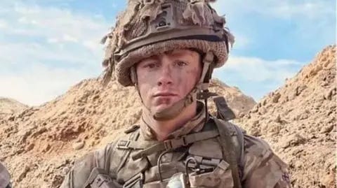 1 Royal Welsh Jack in full combat gear with a jacket and camouflaged helmet in desert colours wiht steep desert mountains in the background