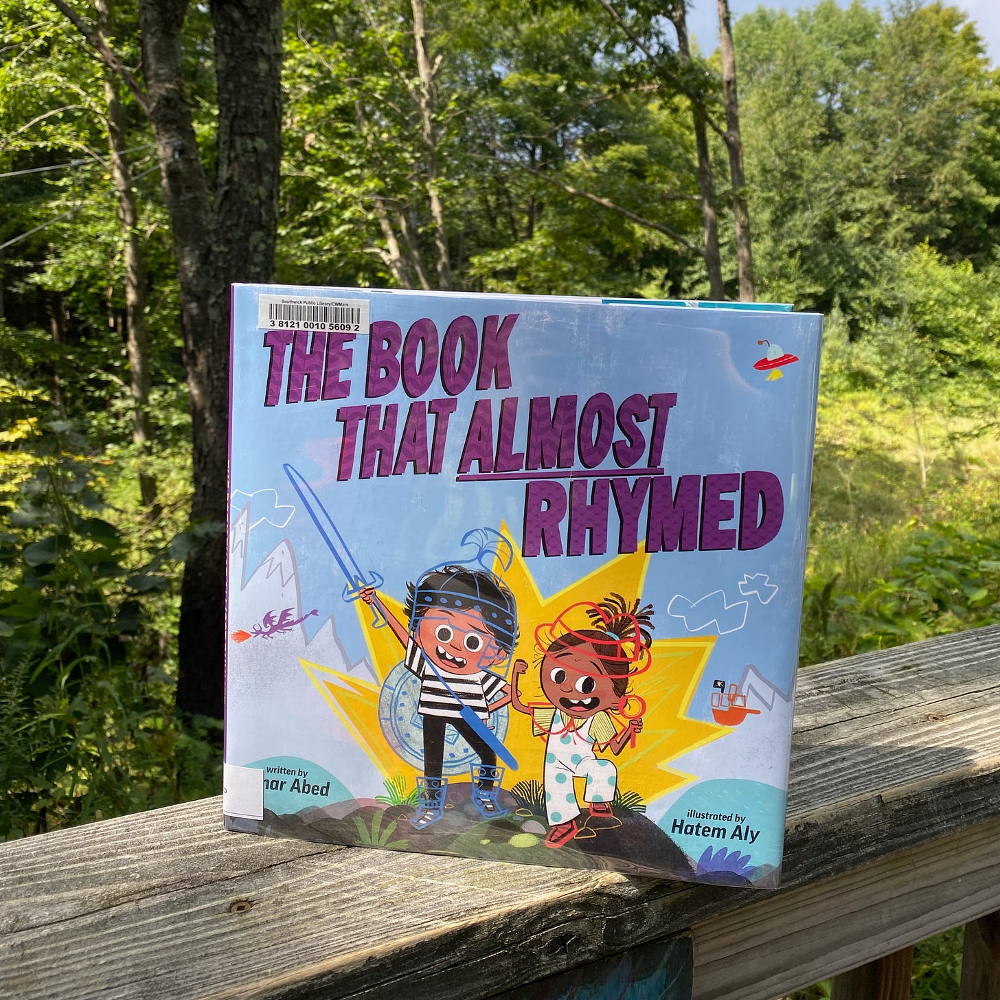 The Book That Almost Rhymed perched on a porch railing in front of some trees.