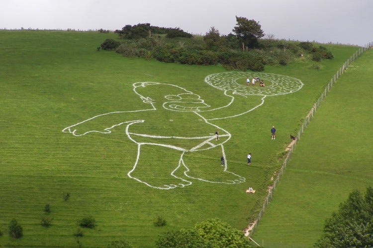 A photo of a gigantic homer simpson in Y fronts brandishing a donut, painted white on a Dorset hillside
